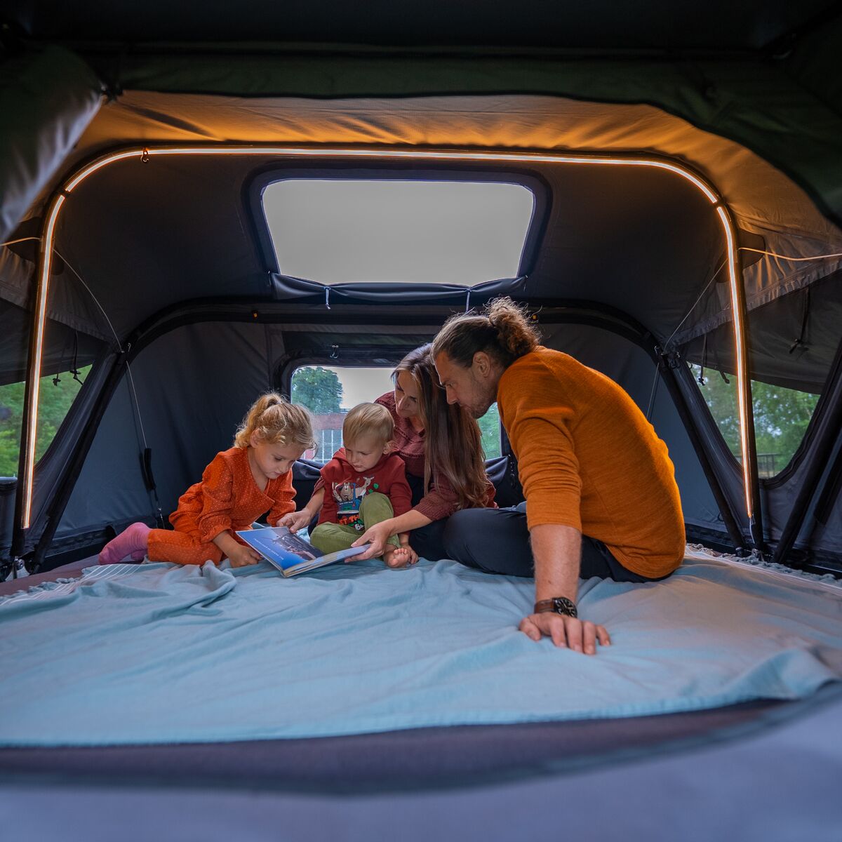 Familie liest gemeinsam im Innenraum des Roof Space 4 Dachzelts