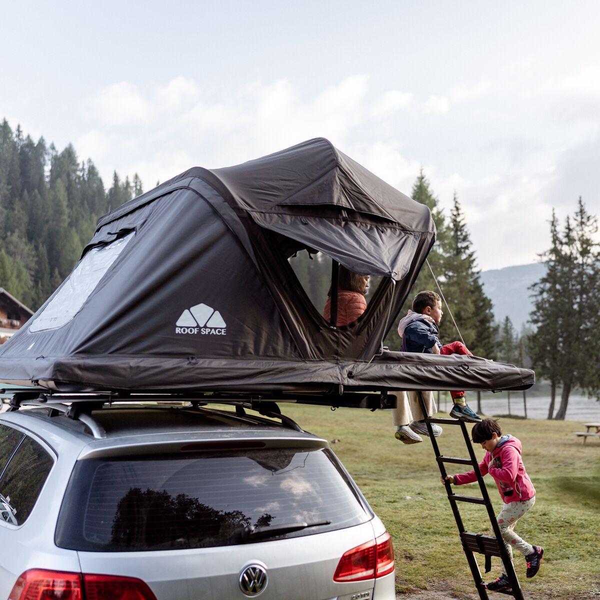 Geöffnetes Roof Space 4 Dachzelt auf einem Kombi am Bergsee, Kinder klettern die Leiter hoch